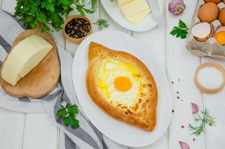 Ajarian Khachapuri traditional Georgian cheese pastry with eggs and butter on a plate on a white wooden background. Homemade baking.の写真素材