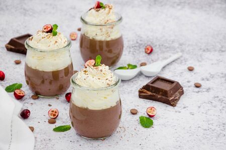 Chocolate cream (pudding, jelly, panna cotta) on agar agar with whipped cream on top in glass jars on a light stone background.の写真素材