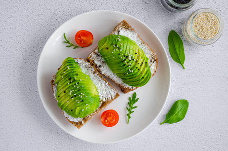 Avocado sandwich on dark rye toast bread made with fresh sliced avocado, cream cheese and seeds on a...