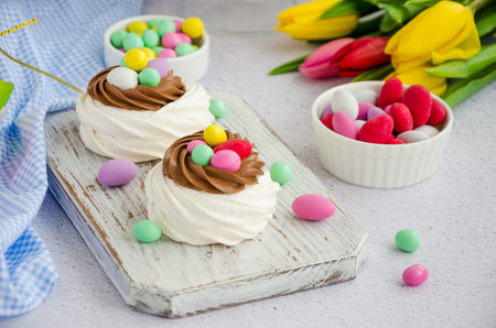 Mini Pavlova Birds Nest with chocolate cream and colored candy on a board on a light background....