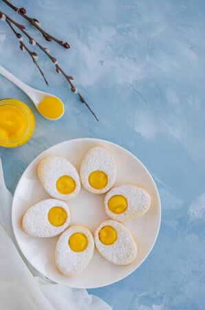 Easter cookies in the form of Easter egg with powdered sugar and lemon cream on a white plate on a light blue concrete background. A greeting card. Easter background. Vertical, Copy space. Top viewの写真素材