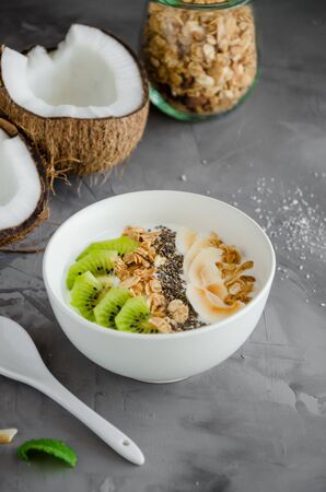 Homemade coconut yogurt in a bowl of granola, kiwi slices, chia seeds and crispy coconut chips. Healthy breakfast. Vegan food. Vertical orientationの写真素材