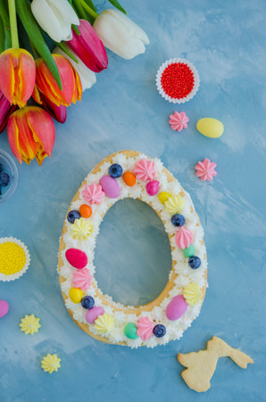 Easter cake egg shaped with cream, candy eggs, cookies, meringue and sprinkles on top on a light...