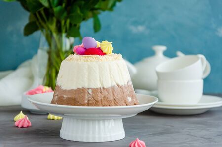 Easter cake. Cottage cheese Easter Paskha Three chocolates with coconut and candy eggs on top on a white plate on a concrete background with flowers. Horizontal orientation. Copy spaceの写真素材
