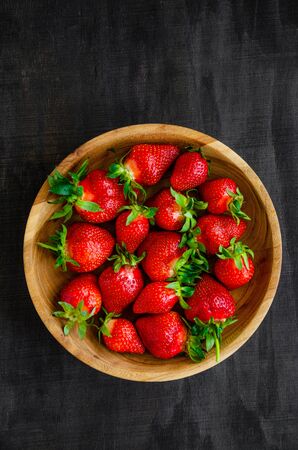Fresh strawberries in a wooden bowl on a dark wooden background. Vertical, copy spaceの写真素材