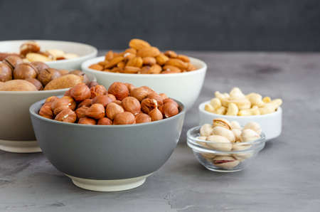 Hazelnuts, almonds, Brazilian nuts, cashews, macadamia, pecans and pistachios in bowls on a dark concrete background. Healthy food. Horizontal, copy spaceの写真素材