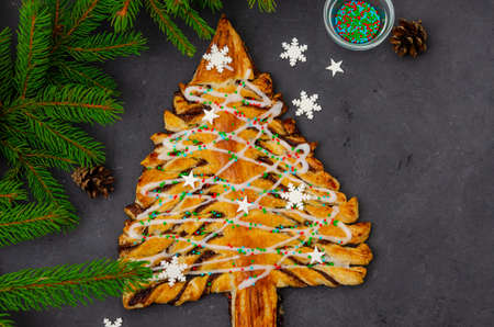 Puff pastry cake or pie with chocolate and cinnamon in shape of Christmas tree on a dark background. Festive cake. Top view, copy spaceの写真素材