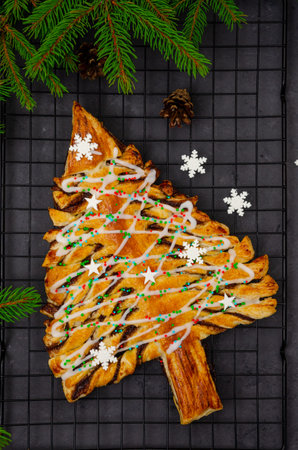 Puff pastry cake or pie with chocolate and cinnamon in shape of Christmas tree on a dark background....