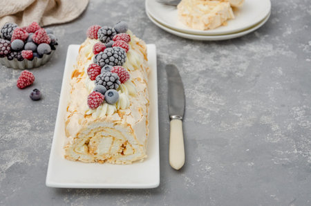 Meringue roll Pavlova cake with cream and raspberries, blackberries and blueberries on top on a gray...