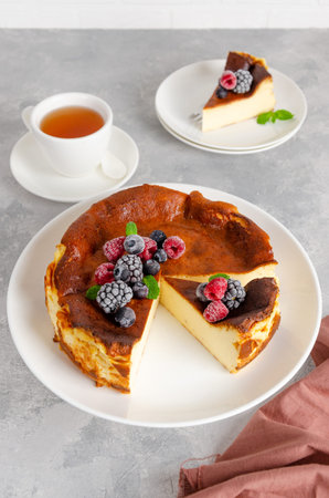 San Sebastian cheesecake with berries and mint leaves on top on a white plate on a gray concrete...