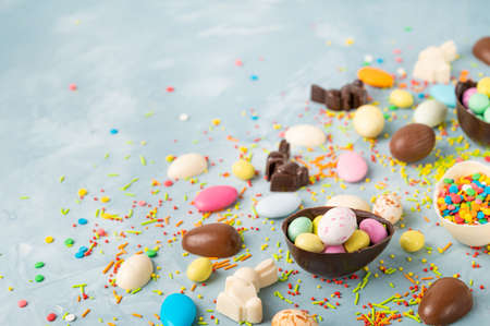 Delicious chocolate easter eggs, rabbits and sweets on a blue concrete background. Easter composition. Copy spaceの写真素材