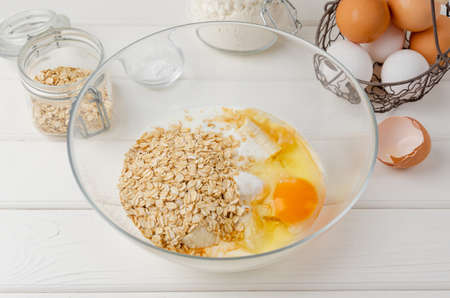 Cooking oatmeal pancakes with bananas. Eggs, buttermilk, sugar, vanilla, oatmeal in a bowl on a white wooden background. Recipe step by stepの写真素材