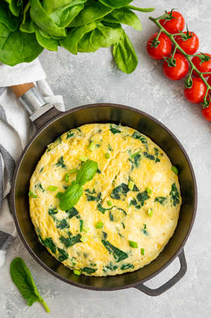Omelette with spinach, green onions and feta cheese in a cast-iron frying pan on a gray concrete background. Healthy breakfast. Top view, copy spaceの写真素材