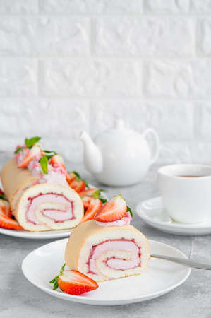 Cake roll with fresh strawberries, jam and cream cheese on a white plate on a gray background. Copy spaceの写真素材