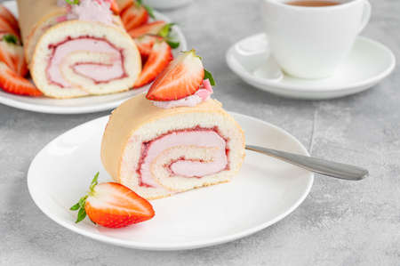 Cake roll with fresh strawberries, jam and cream cheese on a white plate on a gray background. Copy spaceの写真素材