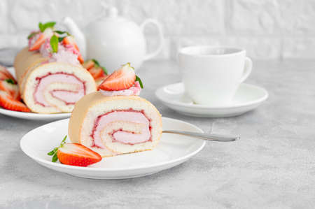 Cake roll with fresh strawberries, jam and cream cheese on a white plate on a gray background. Copy spaceの写真素材