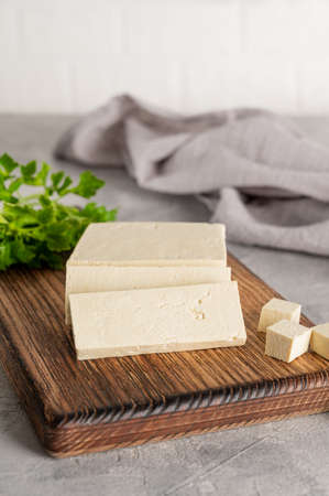Fresh cheese tofu from soybeans with parsley on a board on a gray concrete background. A vegan product. Copy spaceの写真素材