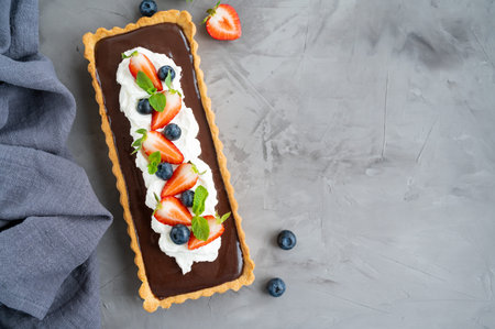 Chocolate cream tart with whipped cream, fresh blueberries and strawberries on top on a dark...