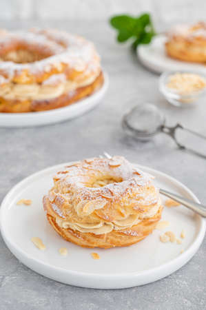 French traditional cake Paris Brest with praline cream, powdered sugar and almond petals on top on a gray concrete background. Copy spaceの写真素材