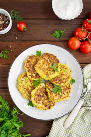 Vegetable zucchini pancakes with cheese, dill and parsley on a plate with sour cream on a dark wooden background. copy space.の写真素材