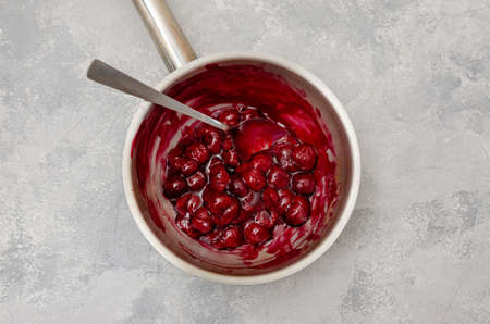 Cherry cooked with sugar and starch in a saucepan to make chocolate roll cake Black forest on a gray concrete background. Recipe step by step. Top viewの写真素材