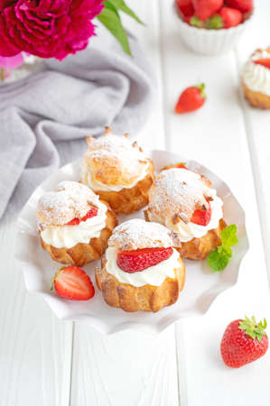 Delicious homemade small cakes profiterole choux pastry with custard, strawberry and icing powder on the white wooden background. Copy spaceの写真素材