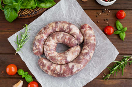 Raw sausages on paper with spices and fresh herbs on a dark wooden background. Top view, copy spaceの写真素材