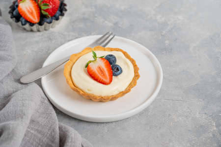Delicious mini tarts with fresh berries and custard on a white plate on a gray concrete background. Copy space.の写真素材