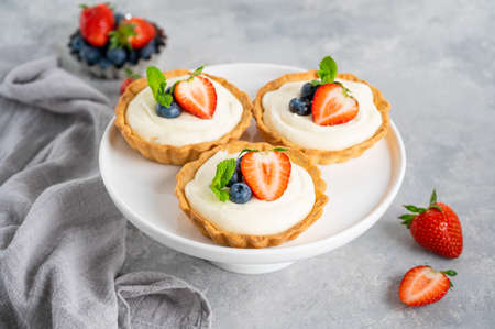 Delicious mini tarts with fresh berries and custard on a white plate on a gray concrete background. Copy space.の写真素材