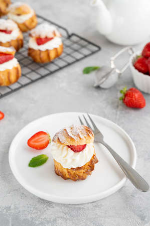 Delicious homemade small cakes profiterole choux pastry with custard, strawberry and icing powder on a gray concrete background. Copy spaceの写真素材