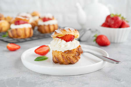 Delicious homemade small cakes profiterole choux pastry with custard, strawberry and icing powder on a gray concrete background. Copy spaceの写真素材