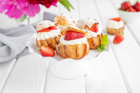 Delicious homemade small cakes profiterole choux pastry with custard, strawberry and icing powder on the white wooden background. Copy spaceの写真素材