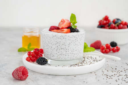 Vanilla chia pudding with fresh berries and honey in a glass on a gray concrete background. Superfoods concept. Copy spaceの写真素材