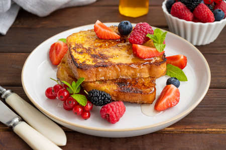 A stack of French toast on a plate with fresh berries, almond petals and honey on a dark wooden background. Delicious breakfast. Copy spaceの写真素材