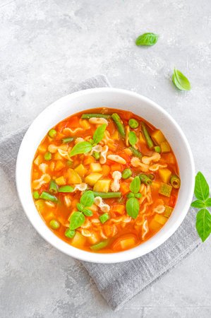 Minestrone soup of fresh vegetables and pasta in a bowl on a gray concrete background. Vegan dish....