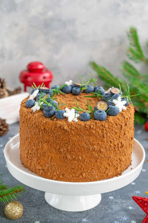 Chocolate honey cake decorated with fresh blueberries, rosemary and sugar snowflakes on top of a white stand. Cake for Christmas and New Year. selective focus.の写真素材