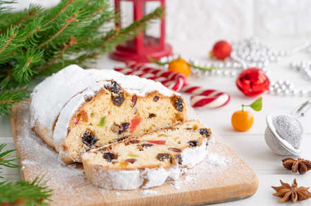 Christmas stollen with dried fruits and powdered sugar on a board on a white wooden background. Copy spaceの写真素材