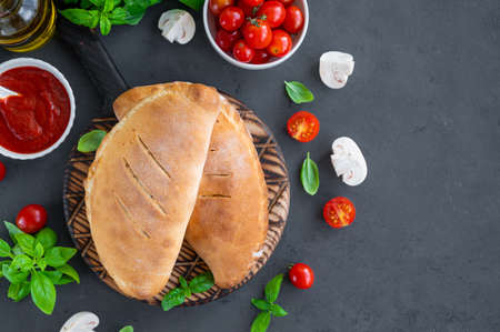 Traditional closed Italian calzone pizza with tomato sauce, mozzarella cheese and mushrooms on a board on a dark background. selective focus, top view, copy spaceの写真素材