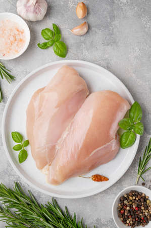 Raw chicken breast or fillet with salt, pepper and fresh herbs on a white plate on a gray background. Health food. top view, copy spaceの写真素材