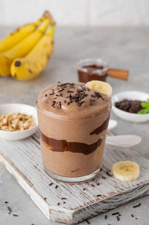 Vegan banana chocolate ice cream with chocolate glaze and sprinkles in a glass on a gray concrete background. Health food. copy spaceの写真素材