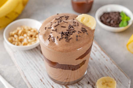 Vegan banana chocolate ice cream with chocolate glaze and sprinkles in a glass on a gray concrete background. Health food. copy spaceの写真素材