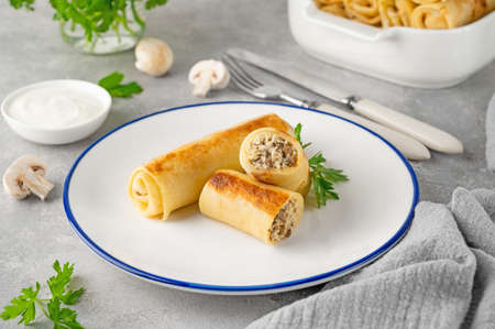 Pancakes or thin crepes stuffed with chicken and mushrooms on a plate on a gray concrete background. selective focus, copy spaceの写真素材