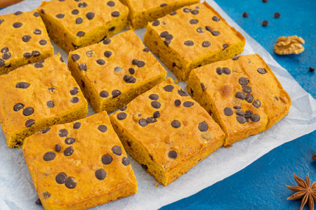 Pumpkin blondie or cake with chocolate drops, walnuts, cinnamon and anise on baking paper on a blue...