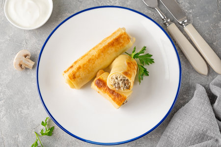 Pancakes or thin crepes stuffed with chicken and mushrooms on a plate on a gray concrete background. Selective focus, copy spaceの写真素材