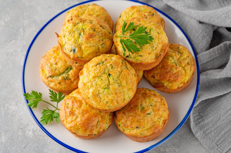 Homemade zucchini muffins with cheese, garlic and herbs on a plate on a gray concrete background. Vegetarian dish. copy spaceの写真素材