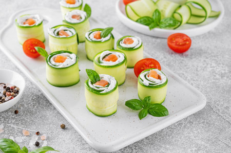 Cucumbers rolls with cream cheese, salted salmon and fresh herbs served on a white ceramic board on a concrete background. Selective focus.の写真素材