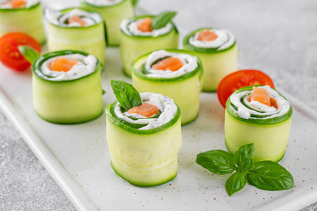 Cucumbers rolls with cream cheese, salted salmon and fresh herbs served on a white ceramic board on a concrete background. Selective focus.の写真素材