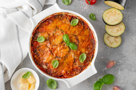 Eggplant casserole with cheese and tomato sauce in a white baking dish on a gray concrete background with ingredients for cooking. Vegetarian healthy foodの写真素材