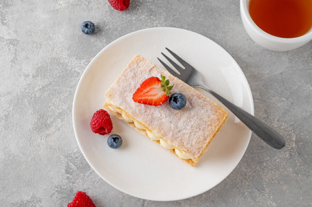 Traditional French dessert millefeuille with vanilla cream and fresh berries on a white plate on a gray concrete backgroundの写真素材