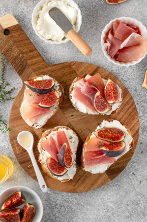 Bruschetta or toast with goat cheese spread, prosciutto, figs and honey on a boardの写真素材